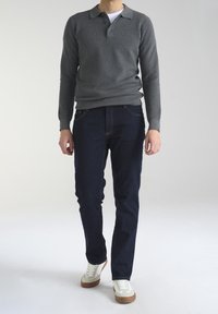 Polo shirt grigio a maniche lunghe con texture, jeans scuri in denim e sneaker bianche con suola marrone. L'outfit è casual e aderente.