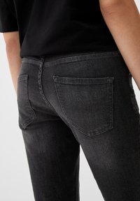 Jeans de mezclilla negra con bolsillos traseros, un diseño ajustado y una sutil textura deslavada. Costura visible a lo largo de los bolsillos y la cinturilla.