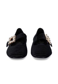 Zapatos de tela negra con textura acanalada, con una banda central y una gran hebilla adornada con un cristal en la parte frontal. Suela plana, punta redondeada.