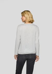 Light gray long-sleeve shirt in soft fabric with a round neckline and straight hem, worn with dark jeans. Simple, minimalistic design.