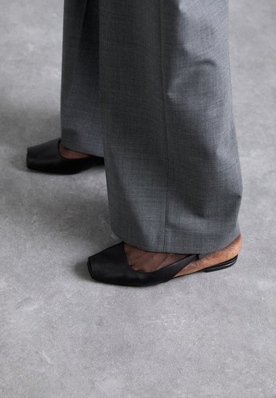 Svarta läderballerinas med fyrkantig tå, med ett utskärningsdesign på sidan och en låg klack, tillsammans med grå vida byxor.