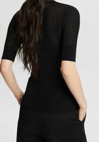 Top corto a coste nero, con maniche corte, caratterizzato da un design aderente, tessuto testurizzato e una cintura aderente, abbinato a pantaloni scuri.