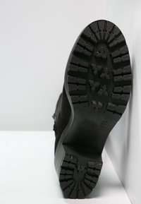 Suela de bota negra con un patrón de banda de rodadura texturizado y resistente. Hecha de goma, cuenta con profundas ranuras para tracción y estabilidad. Diseño de tacón redondeado.