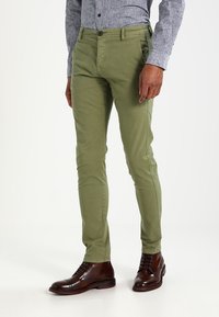 Gröna bomullschinos med smal passform, med knappstängning, fram- och bakfickor, samt en mjuk textur. Bärs ihop med bruna läderstövlar.