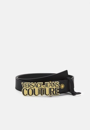Cintura in pelle nera con grande fibbia dorata che mostra il logo "Versace Jeans Couture" in caratteri in grassetto.
