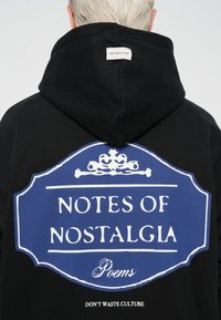Zwarte hoodie met een blauw grafisch ontwerp featuring "NOTES OF NOSTALGIA" en "Poems." Inclusief label "DON'T WASTE CULTURE" op de achterkant.