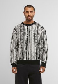 Schwarzer und grauer gemusterter Pullover mit vertikalen Streifen, gerippten Bündchen und Saum sowie einem runden Halsausschnitt. Hergestellt aus strukturiertem Strickmaterial.