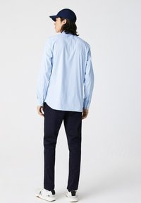 Camicia azzurra a maniche lunghe con colletto abbottonato, abbinata a pantaloni blu navy e sneakers bianchi. Design semplice e pulito, orlo leggermente curvo.