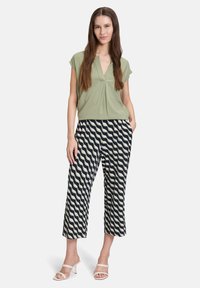 Blouse vert clair avec un col en V et des plis, associée à un pantalon court à motifs navy avec des rayures blanches ondulées. Porté avec des sandales à talons nudes.