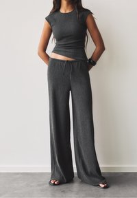Crop top gris à côtes avec manches courtes associé à un pantalon large taille haute. Texture lisse et détail de cordon à la taille.