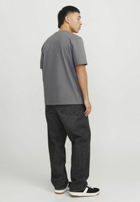 Grijze shirt met korte mouwen en een ronde hals, gecombineerd met donkergrijze loszittende jeans en zwarte sneakers met witte accenten.