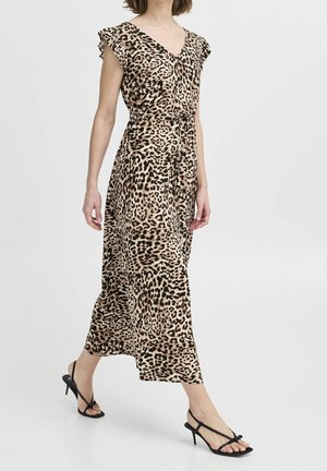 Kobieta idąca w bezrękawną sukienkę w panterkę sięgającą kostek, z dekoltem w kształcie litery V, wiązaną w talii oraz czarnymi sandałami na obcasie.