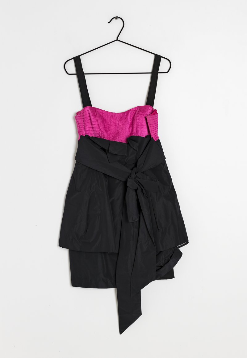 Robe sans manches noire et rose avec un corsage rose texturé, un tissu drapé noir et un grand nœud sur le côté, suspendue à un cintre noir.