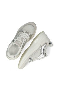 Bílé tenisky s síťovanou tkaninou, stříbrnými akcenty a texturovanou podrážkou. Mají bílé tkaničky a logo na jazyku a stélce.