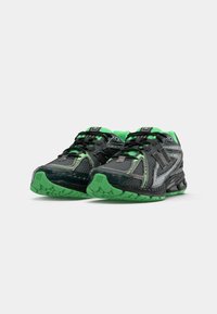 Des chaussures de sport noires et vertes avec une tige en mesh, une semelle en caoutchouc et des accents contrastants en argent et en vert vif. Elles disposent d'un système de laçage complexe.