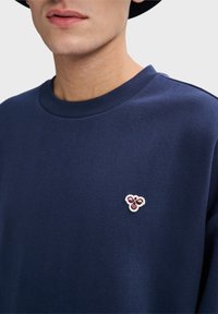 Navyblauwe sweatshirt met een ronde hals en geribbelde manchetten, voorzien van een klein geborduurd logo op de borst. Zachte stofstructuur.