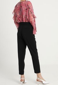 Blusa de flores rosa de manga larga con mangas con volantes, combinada con pantalones negros ajustados y zapatos de tacón blancos, vista desde la espalda.