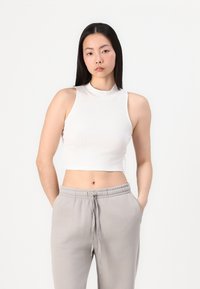 Valge lühike tank top, millel on kõrge kaelus, sooniline tekstuur ja ilma varrukateta disain, koos hallide elastse vöökohtaga pükstega.