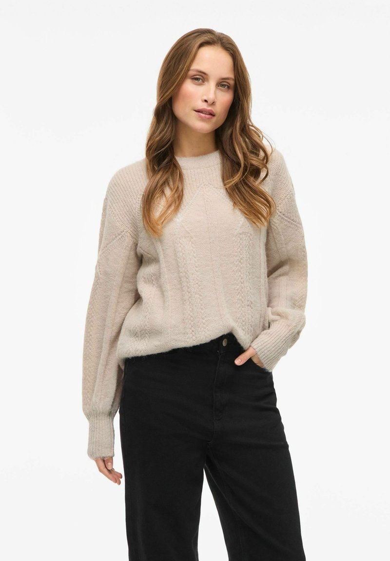 Hellbeige gestrickter Pullover mit einem strukturierten Muster; lockere Ärmel, Rundhalsausschnitt und getragen mit schwarzen hoch taillierten Hosen.