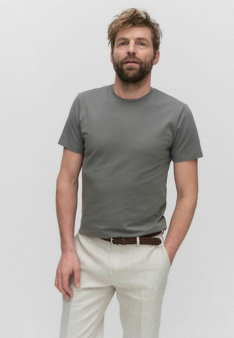 Grijze ronde hals t-shirt van een zachte stof, gecombineerd met licht beige broeken. Heeft korte mouwen en een relaxte pasvorm.