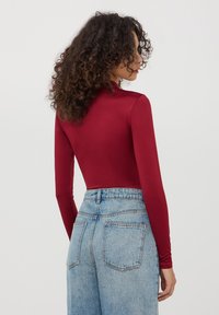 Body a maniche lunghe in tessuto bordeaux con design aderente, abbinato a jeans azzurri a vita alta con tasche posteriori.