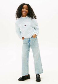 Jasnoniebieski sweter z napisem "HILFIGER", falbaniastym kołnierzykiem, w połączeniu z jasnoniebieskimi spodniami o szerokiej nogawce i czarnymi butami na platformie.