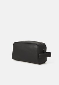Svart lærpung med rektangulær form, glatt tekstur, glidelås og sidehåndtak. Minimalistisk design uten mønstre eller pynteelementer.