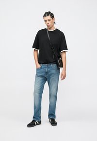 Μαύρο κοντομάνικο μπλουζάκι με λευκή επένδυση, ανοιχτό μπλε τζιν παντελόνι και μαύρα αθλητικά παπούτσια. Το μοντέλο κρατά μια μικρή μαύρη τσάντα χιαστί.