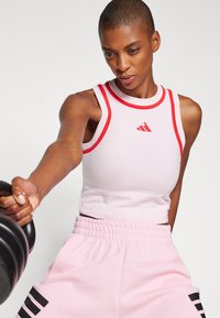 Lichtroze crop top met rode accenten en een klein logo, gecombineerd met hoogopgetrokken roze broek met zwarte strepen en een gathered tailleband.