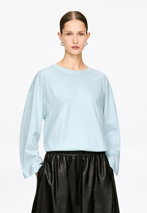 Hellblaues Langarmhemd mit lockerem Schnitt und rundem Ausschnitt, kombiniert mit einem schwarzen Lederrock mit elastischem Bund.