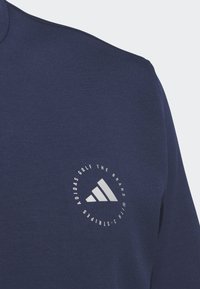 Sudadera de color azul marino con cuello redondo, que presenta un logo circular plateado y un gráfico de tres franjas en el área del pecho izquierdo.