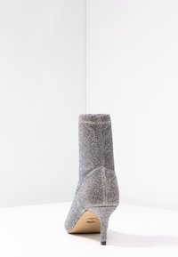 Bottine en tissu gris avec une finition texturée, petit talon aiguille et dessus ajusté. Le talon est fin et effilé.