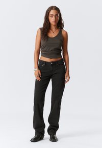 Noor noor, kellel on pikad lokkis juuksed, kannab tumedat ilma varrukateta toppi, musti teksaseid, musti saapaid, hõbedasi käevõrusid, rõngaid ja ripatsikaelakeed.