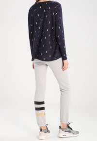 T-shirt à manches longues bleu marine avec un motif d'éclairs blancs, associé à un pantalon de jogging gris comportant des rayures noires et dorées au niveau des poignets et des baskets.