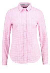 Chemise à manches longues à carreaux roses et blancs avec col et silhouette ajustée, présentée sur un fond uni.