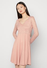 Vestido rosa com corpete rendado e mangas longas, com decote em V e saia rodada, feito de um tecido leve e macio.