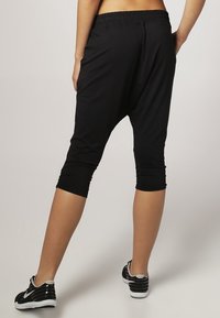 Pantaloni harem neri a vita alta, con un elastico in vita, dal fit morbido, dettagli arricciati alla caviglia e una texture del tessuto liscia.