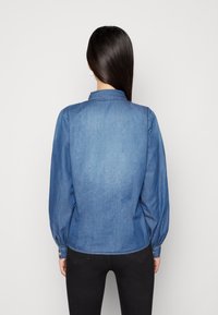 Denim shirt with long sleeves and a collar, medium wash blue color. Features buttoned cuffs and subtle back yoke detail.