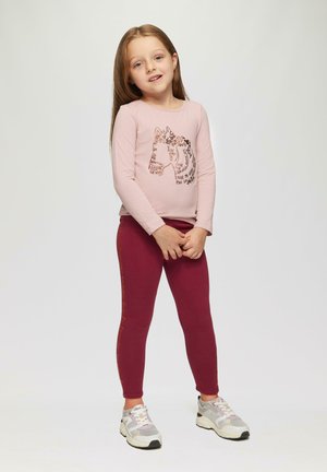 Lichtroze lange mouwen t-shirt met een paardenafbeelding en bruine tekst, gecombineerd met bordeauxrode leggings met oranje letters aan de zijkant.
