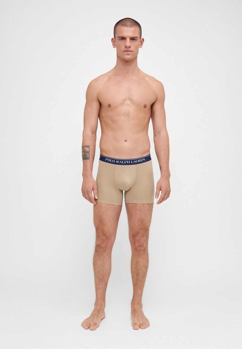 Beige bokserice iz raztegljive tkanine, z modrim pasom na katerega je logo "POLO RALPH LAUREN". Gladka tekstura in prilegajoča zasnova.