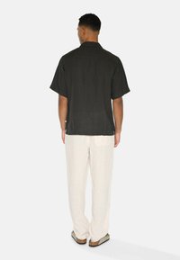 Kurzärmliges, dunkelgraues Shirt aus strukturiertem Stoff, kombiniert mit hellbeigen, locker sitzenden Hosen und grauem Schuhwerk. Einfaches Design, keine Muster.