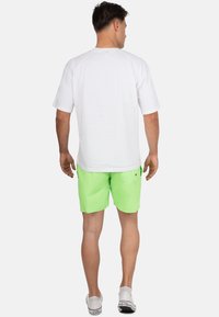 Witte short-sleeve shirt, gecombineerd met felgroene zwemshorts. De shorts hebben een achterzak en een gladde textuur. Witte instapschoenen.