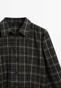 Chemise à carreaux sombre à boutons, manches longues, avec un col pointu et un motif de lignes bleues, brunes et blanches sur fond noir.