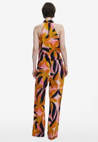 Top con scollatura all'americana e pantaloni palazzo con un motivo floreale, caratterizzati da tonalità di arancione, rosa e verde scuro su uno sfondo rosa chiaro.