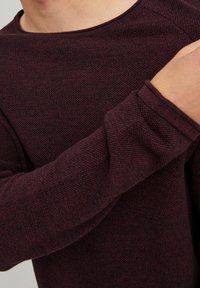 Maglione bordeaux con trama testurizzata, colletto rotondo e maniche lunghe. Il tessuto presenta un fine motivo a intreccio, evidenziando profondità e ricchezza nel colore.