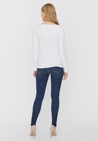 Witte lange mouwen top gecombineerd met donkerblauwe skinny jeans. De jeans hebben standaard achterzakken en een getailleerde pasvorm.
