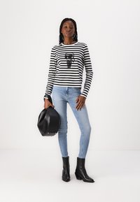 Svart og hvit stripete langermet skjorte med grafisk trykk, pyntet med lyseblå smale jeans og svarte ankelstøvler.