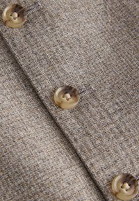Textured brown fabric with two large, translucent buttons featuring a subtle pattern and contrasting thread details.