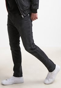 Mustad slim-fit teksased sileda pinnaga, hästi määratletud õmblustega ja klassikalise viie taskuga disainiga. Kombineeritud valgete kanvasist tossudega.