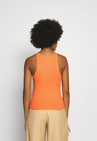 Top de alças laranja canelado com um design ajustado e alças largas, combinado com calças beiges de cintura alta.